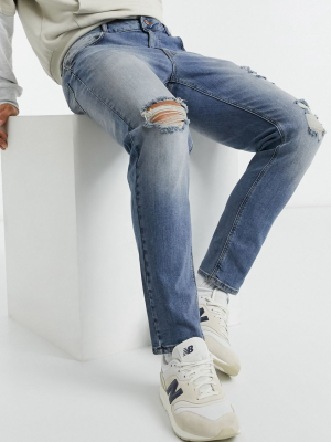 Asos Design Tapered Jeans In Tinted Mid Wash Blue With Knee Rip